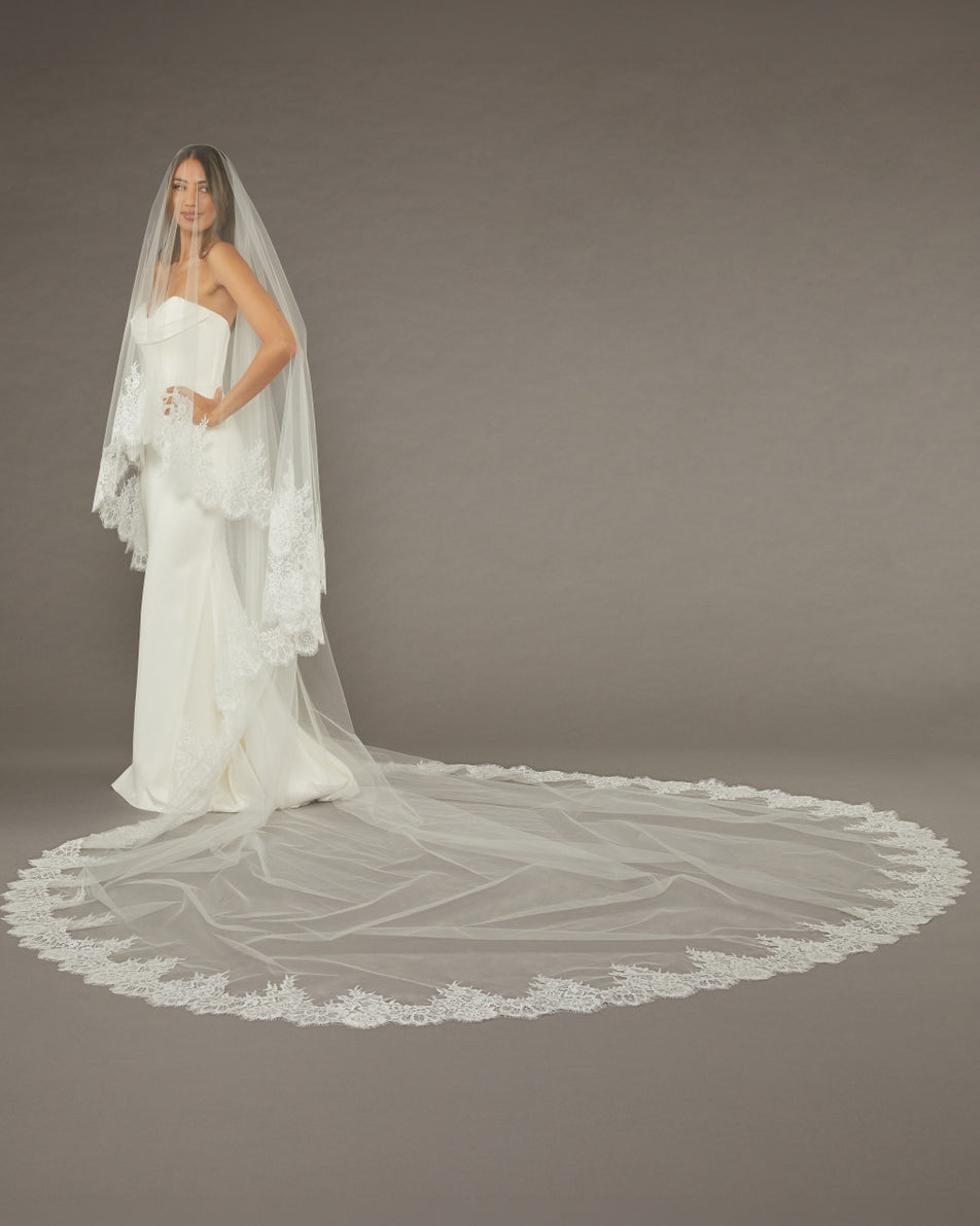 Two Layer Chantilly Lace Cathedral Bridal Veil Bride wearing a long, elegant wedding dress with a matching veil against a plain background