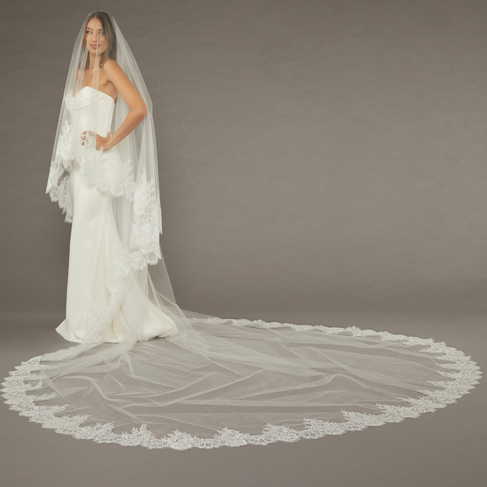 Two Layer Chantilly Lace Cathedral Bridal Veil Bride wearing a long, elegant wedding dress with a matching veil against a plain background