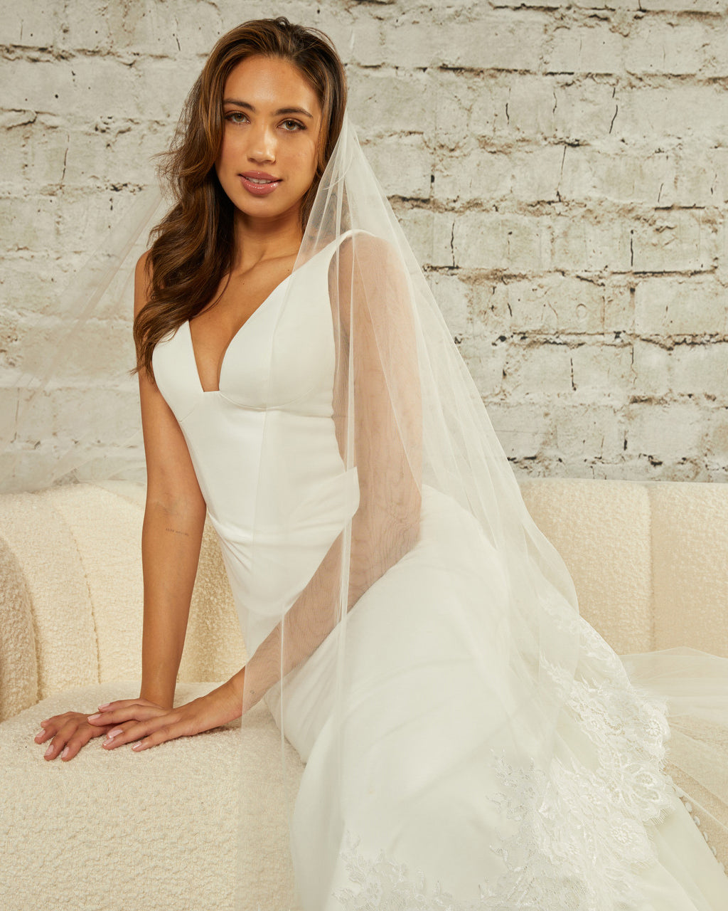 Two Layer Chantilly Lace Cathedral Bridal Veil Woman wearing a wedding dress with a veil against a light brick wall.