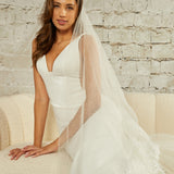 Two Layer Chantilly Lace Cathedral Bridal Veil Woman wearing a wedding dress with a veil against a light brick wall.
