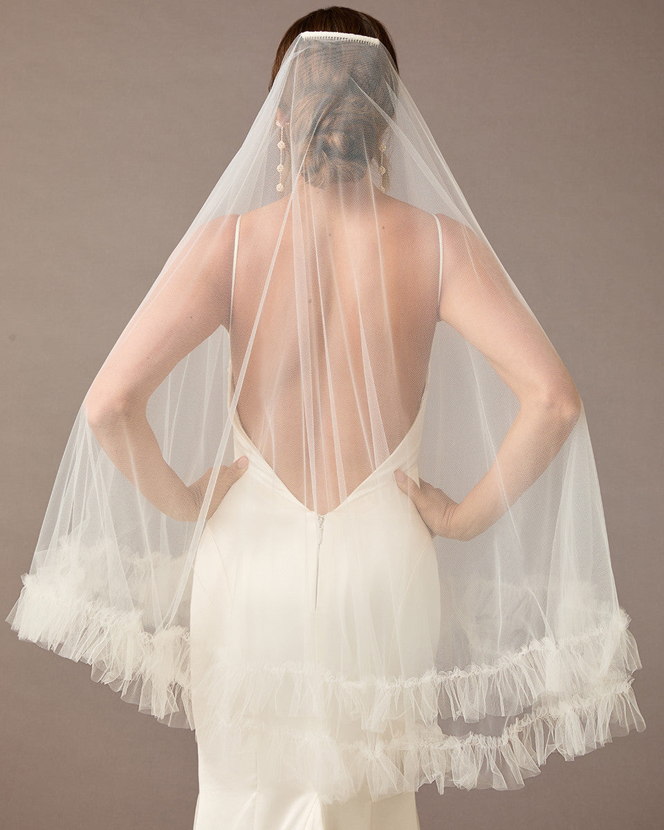 Fingertip Veil of Luxe Tulle with Ruffle Edge Woman wearing a wedding dress with a sheer veil against a brown background