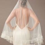 Fingertip Veil of Luxe Tulle with Ruffle Edge Woman wearing a wedding dress with a sheer veil against a brown background