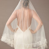 Fingertip Veil of Luxe Tulle with Ruffle Edge Woman wearing a wedding dress with a sheer veil against a brown background