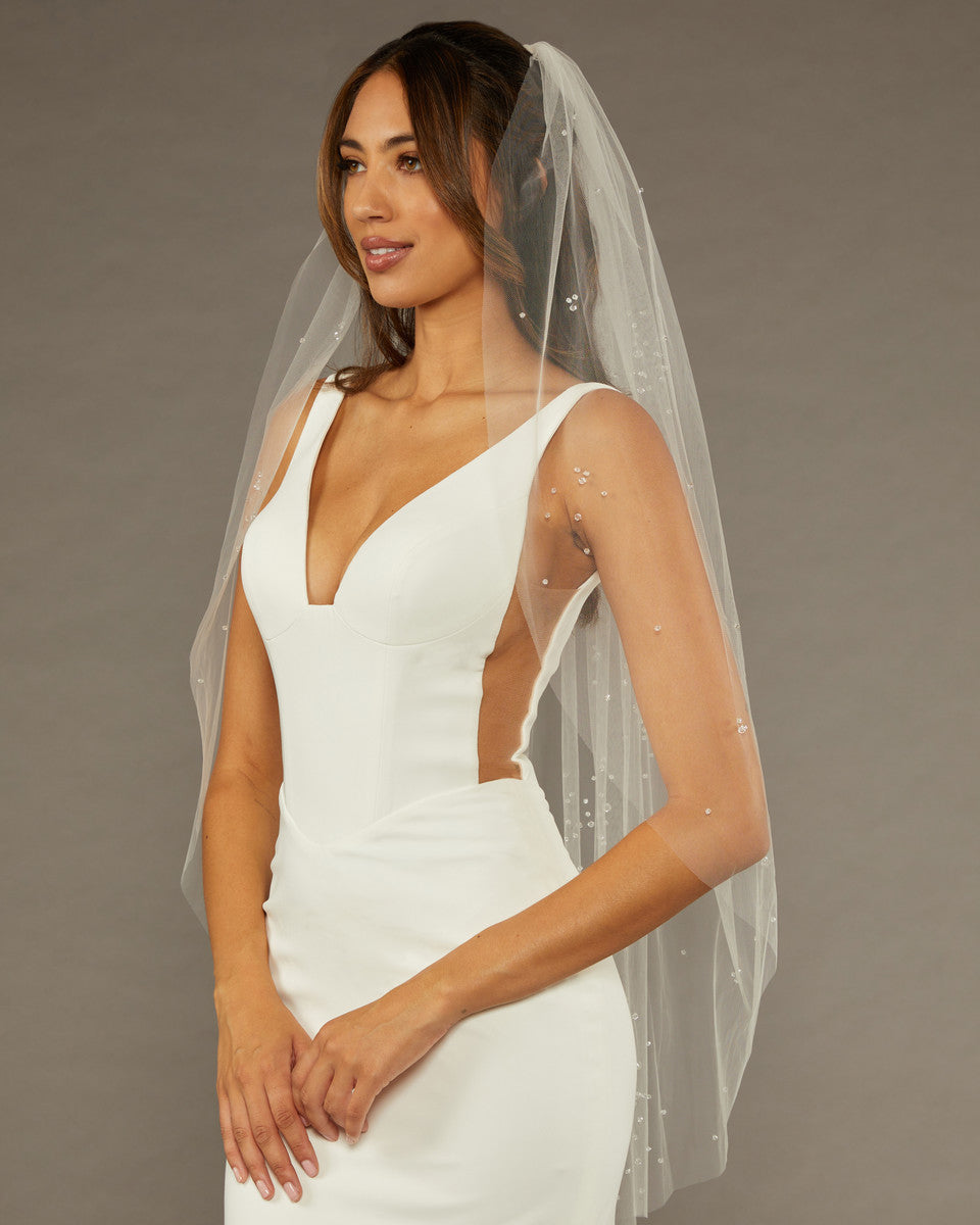 Fingertip Veil with Scattered Clusters of Crystal Beads Woman wearing a wedding dress with a veil against a brown background