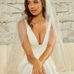 Fingertip Veil with Glitter and Sequins Woman wearing a wedding dress with a veil against a textured wall background