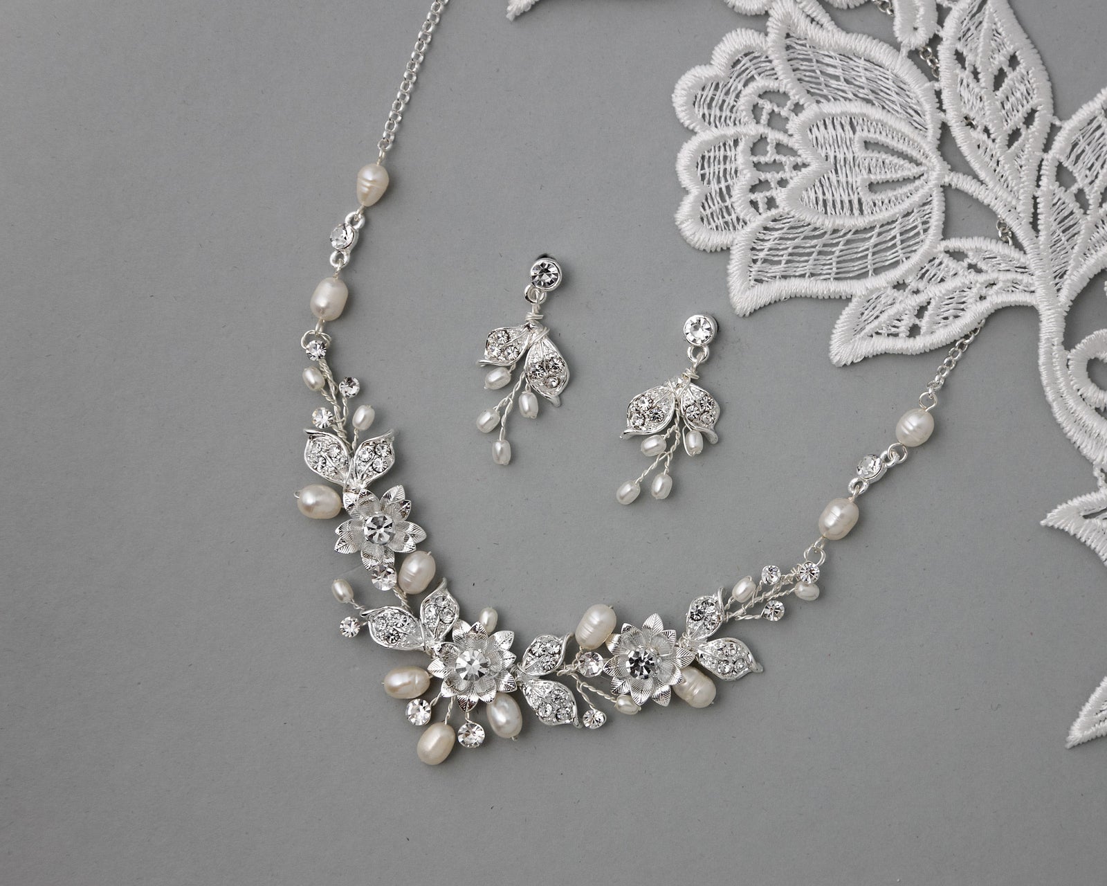 A set of bridal jewelry including a necklace and earrings with metal flowers, rhinestone centers, jeweled leaves, and freshwater pearls.