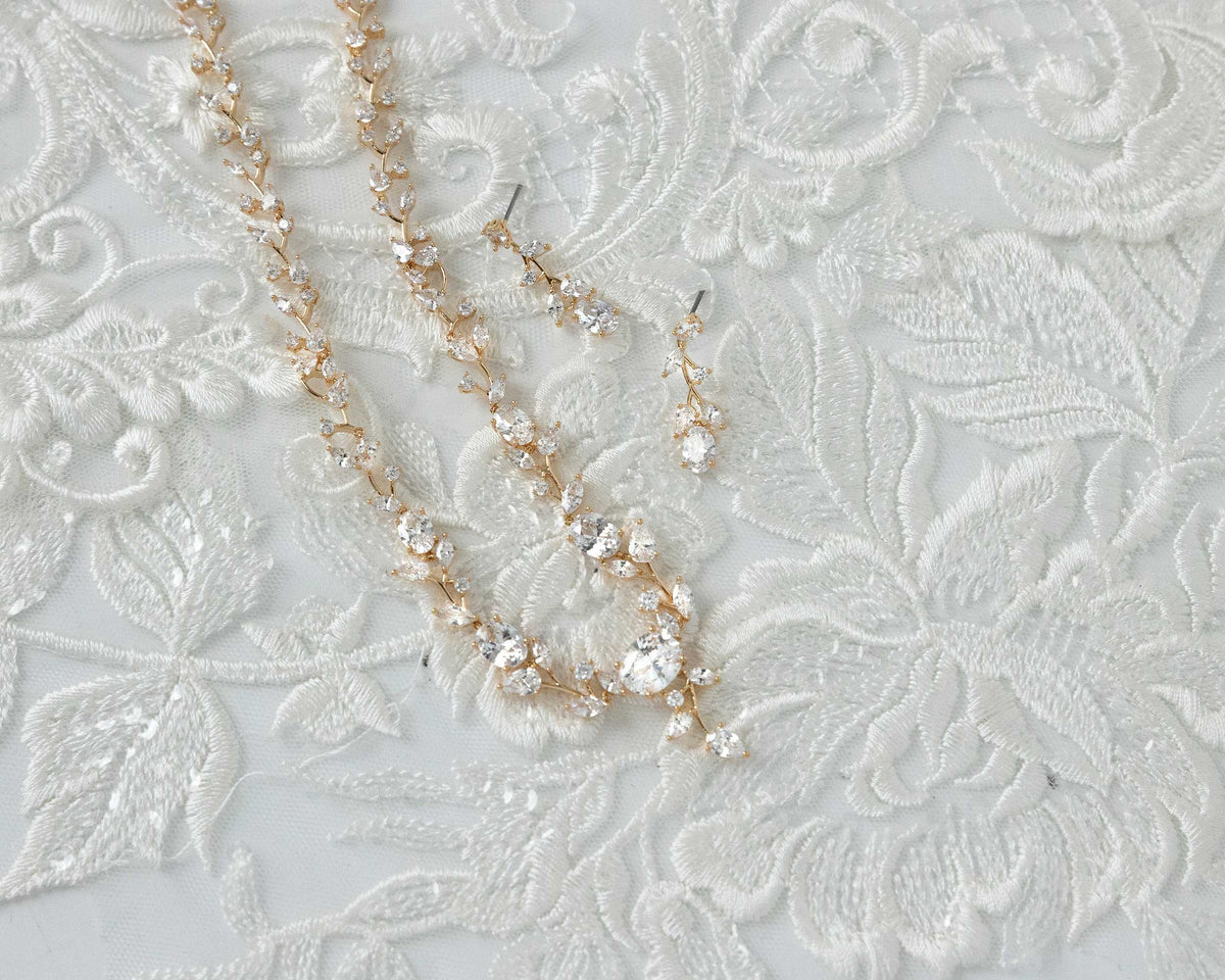 A bridal necklace set with dainty oval vines and sparkling oval CZ gems, displayed on a translucent fabric surface.