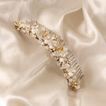 Gold Tiara Comb with Freshwater Pearls A gold bridal hair comb embellished with clear crystals, faux pearls, and delicate gold leaf details, displayed on a draped cream satin fabric.