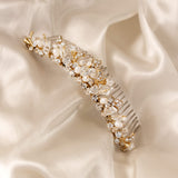 Gold Tiara Comb with Freshwater Pearls A gold bridal hair comb embellished with clear crystals, faux pearls, and delicate gold leaf details, displayed on a draped cream satin fabric.