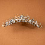 Gold Tiara Comb with Freshwater Pearls A gold floral crown headband embellished with clear crystals and white faux pearls, displayed against a solid warm brown background.