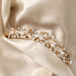 Gold Tiara Comb with Freshwater Pearls A gold floral vine tiara adorned with clear crystals, white faux pearls, and gold-toned leaves, displayed on draped cream satin fabric.
