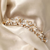 Gold Tiara Comb with Freshwater Pearls A gold floral vine tiara adorned with clear crystals, white faux pearls, and gold-toned leaves, displayed on draped cream satin fabric.
