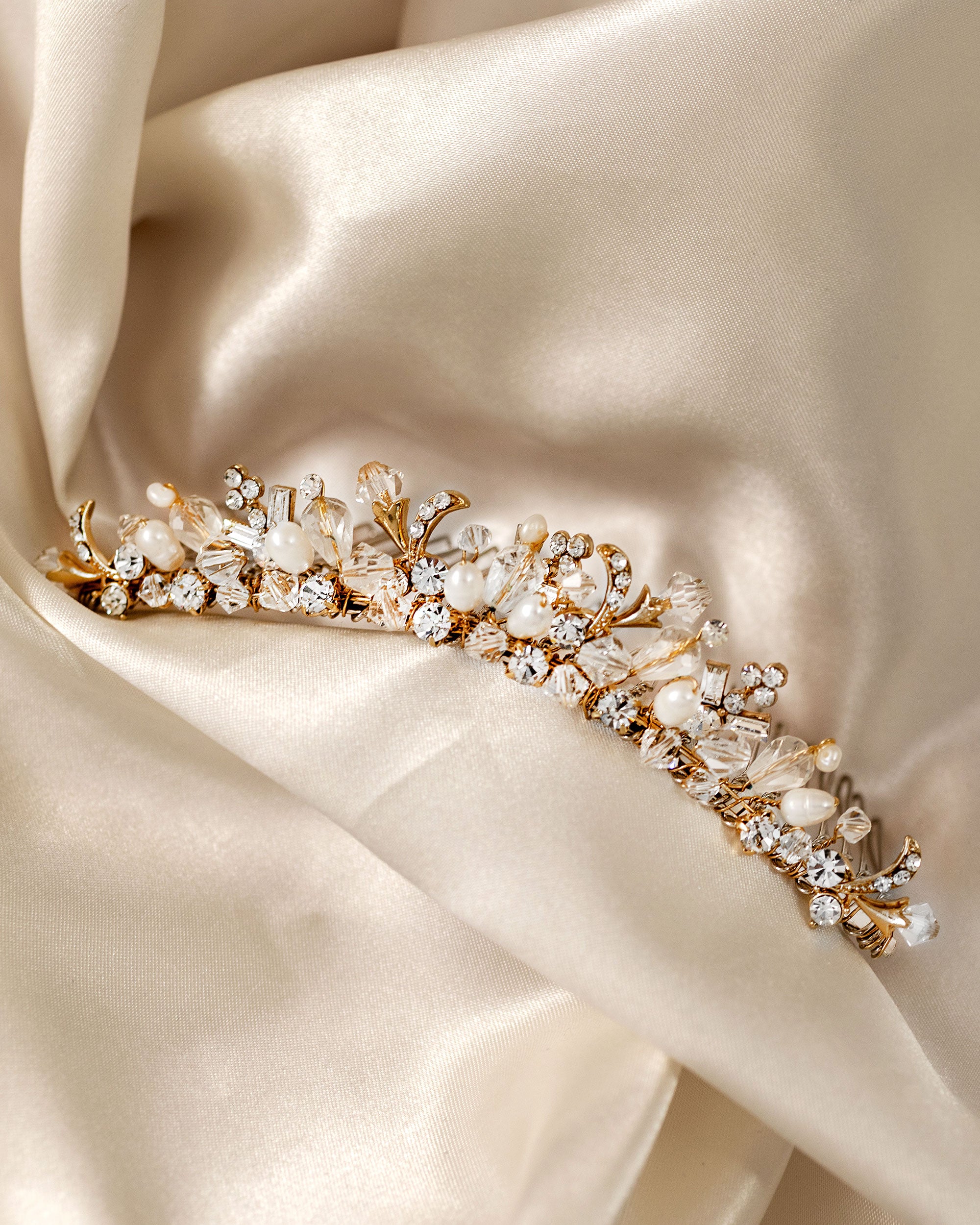 Gold Tiara Comb with Freshwater Pearls A gold floral vine tiara adorned with clear crystals, white faux pearls, and gold-toned leaves, displayed on draped cream satin fabric.