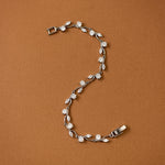CZ Bracelet Marquise and Round Vine A silver vine bracelet with clear marquise and round-cut stones, arranged in an S-shape on a solid brown background.