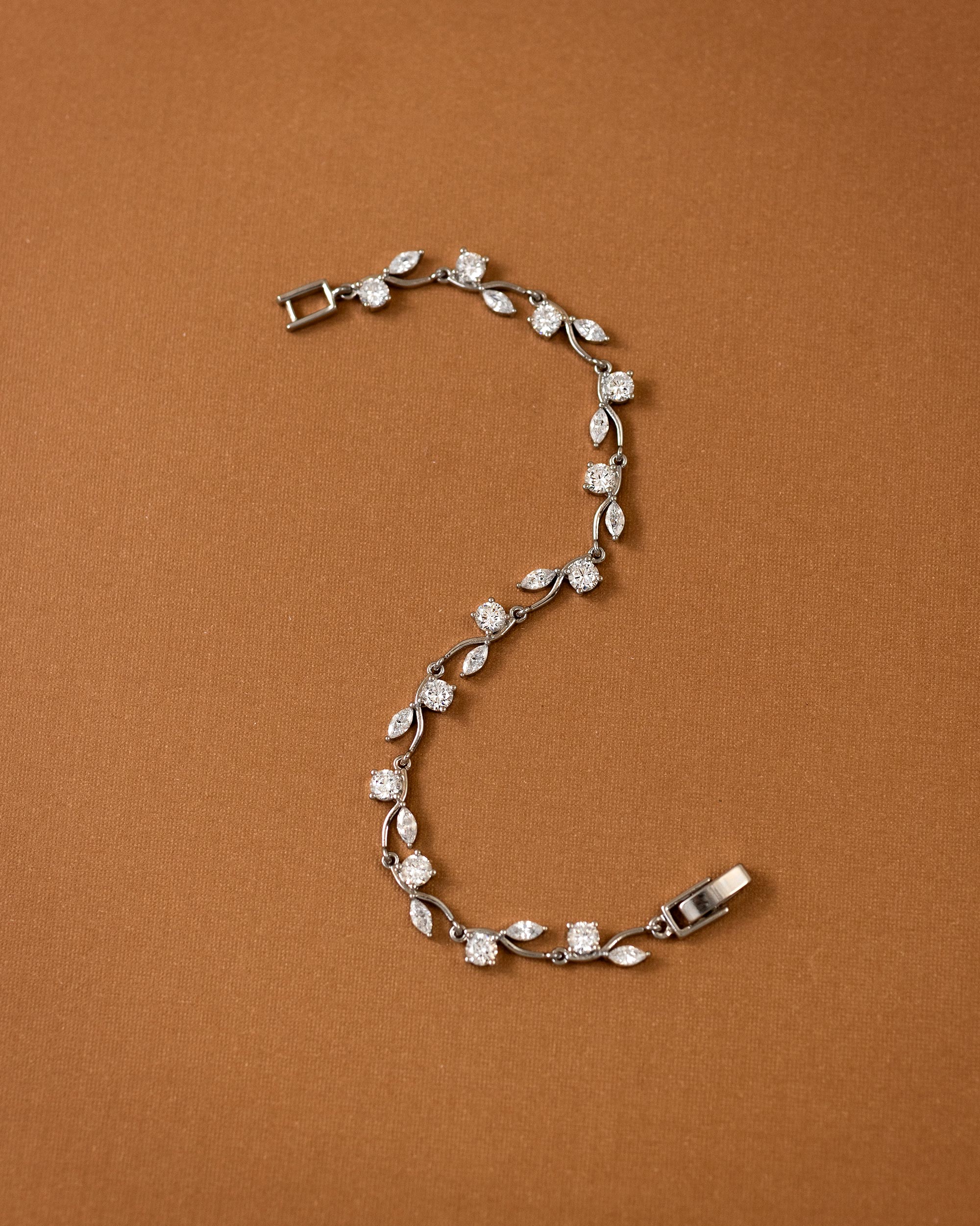CZ Bracelet Marquise and Round Vine A silver vine bracelet with clear marquise and round-cut stones, arranged in an S-shape on a solid brown background.