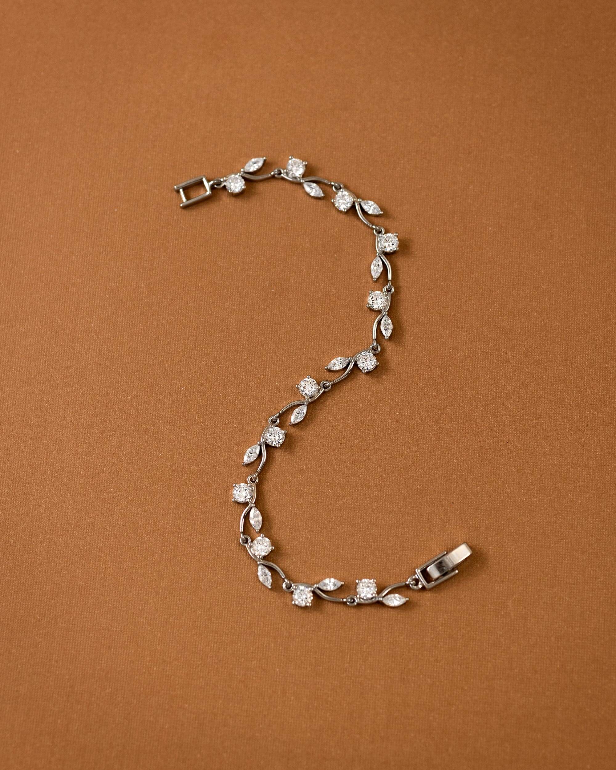 CZ Bracelet Marquise and Round Vine A silver vine bracelet with clear marquise and round-cut stones, arranged in an S-shape on a solid brown background.