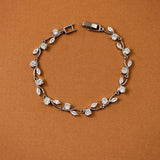 CZ Bracelet Marquise and Round Vine A silver-toned leaf and diamond bracelet arranged in a circle on a textured brown background.