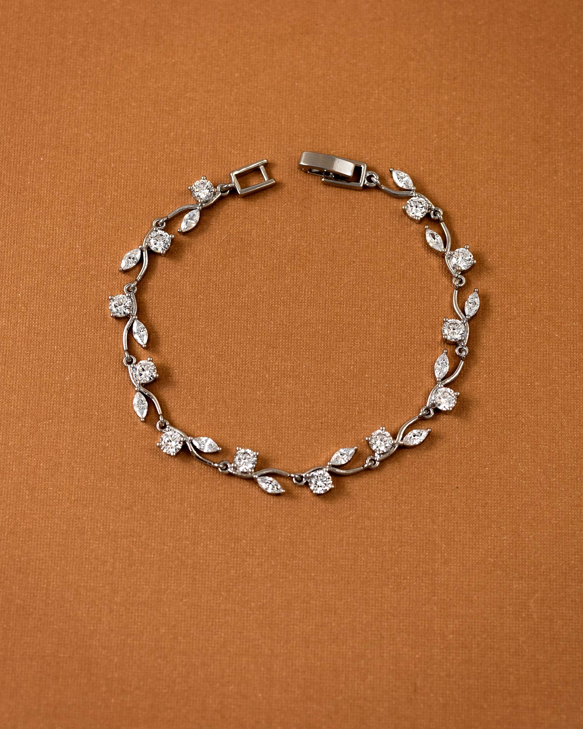 CZ Bracelet Marquise and Round Vine A silver-toned leaf and diamond bracelet arranged in a circle on a textured brown background.
