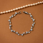 CZ Bracelet Marquise and Round Vine A silver-toned leaf and flower bracelet with clear stones, displayed on a warm brown textured background with a pearl necklace partially visible at the top.