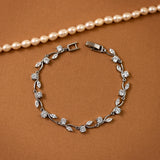 CZ Bracelet Marquise and Round Vine A silver-toned leaf and flower bracelet with clear stones, displayed on a warm brown textured background with a pearl necklace partially visible at the top.