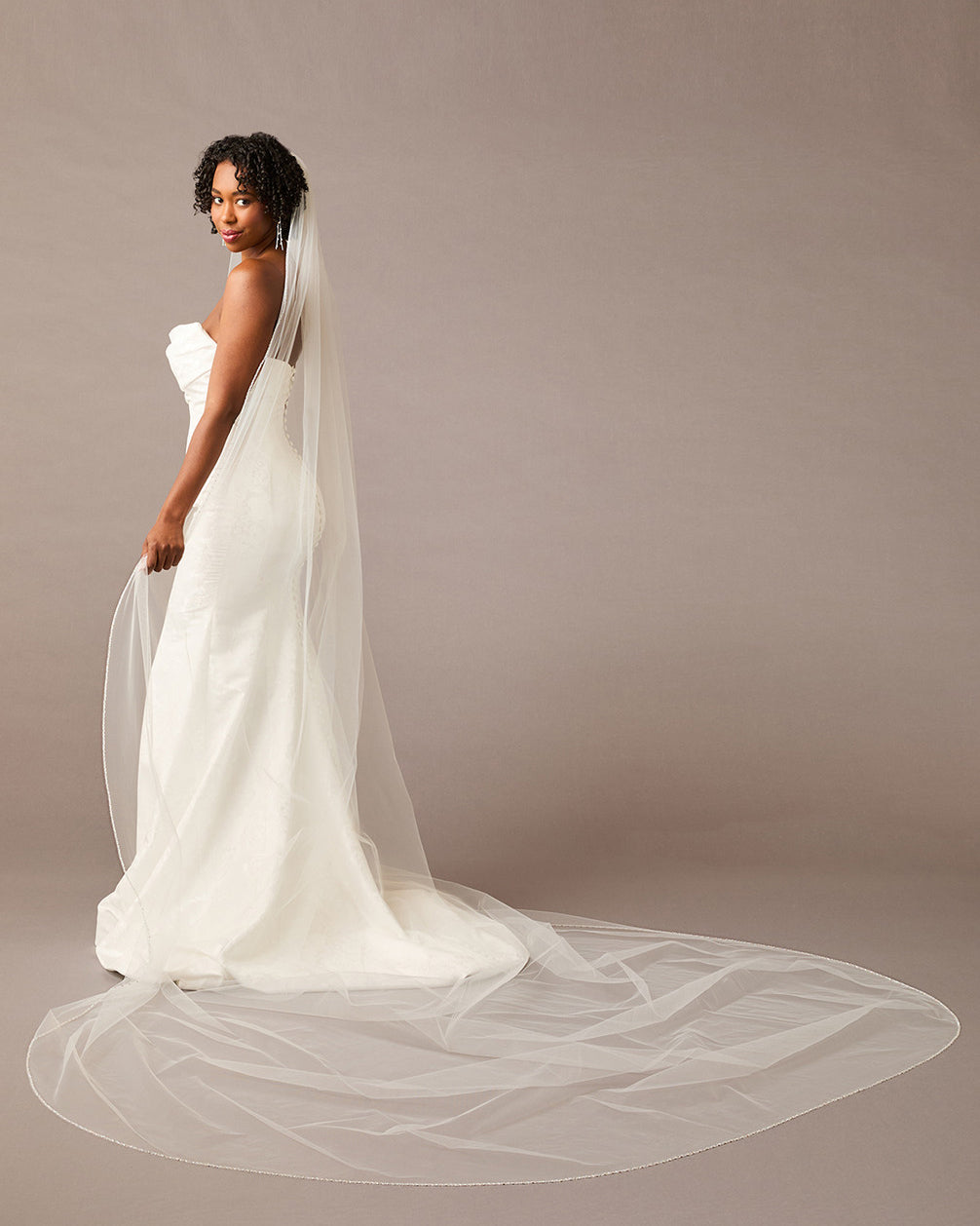 Woman wearing a wedding dress with a long veil against a plain background - Royal Cathedral Bridal Veil with Iridescent Rhinestones- Cassandra Lynne