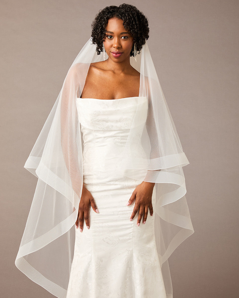 Two Inch Horsehair Trim Waltz Veil Woman wearing awedding dress with a sheer overcoat against a plain background