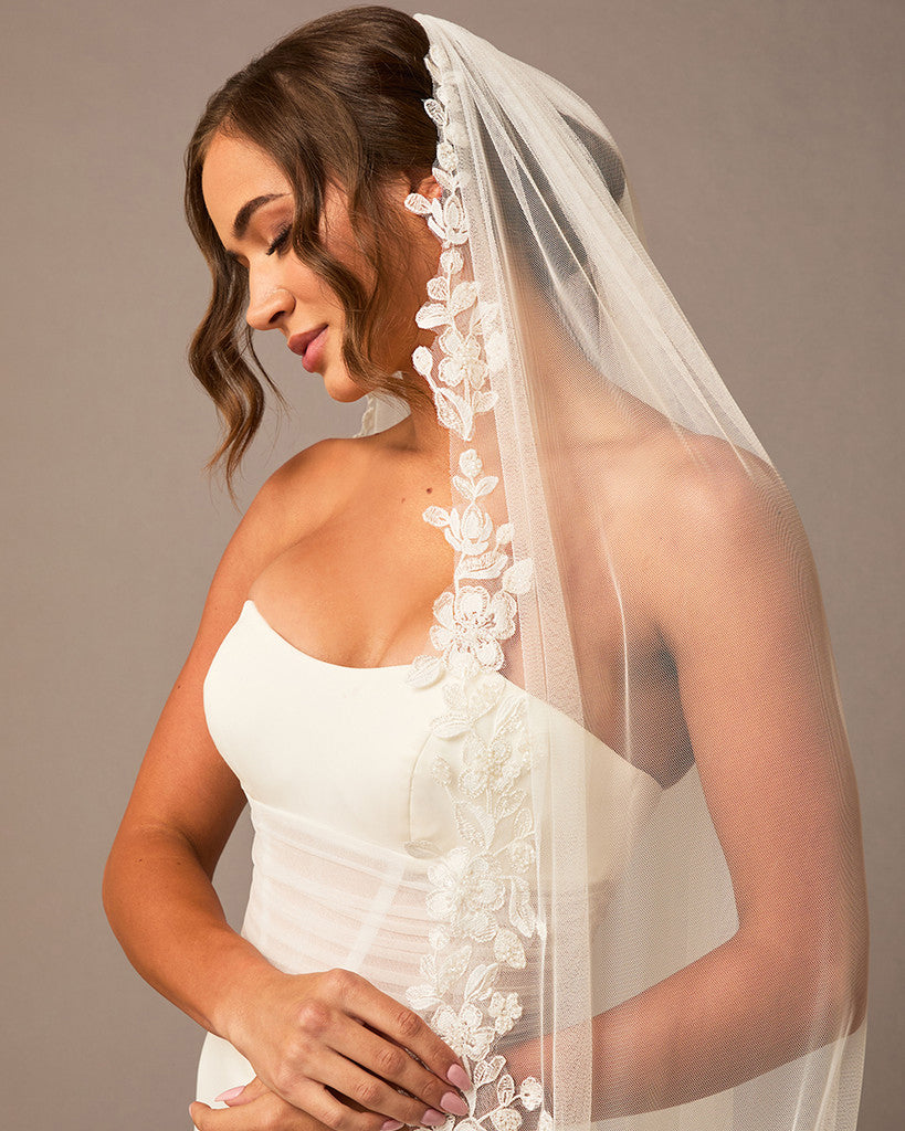 Ivory Luxe Tulle Lace Trim Royal Cathedral Bridal Veil Woman wearing a wedding dress with a lace veil against a neutral background
