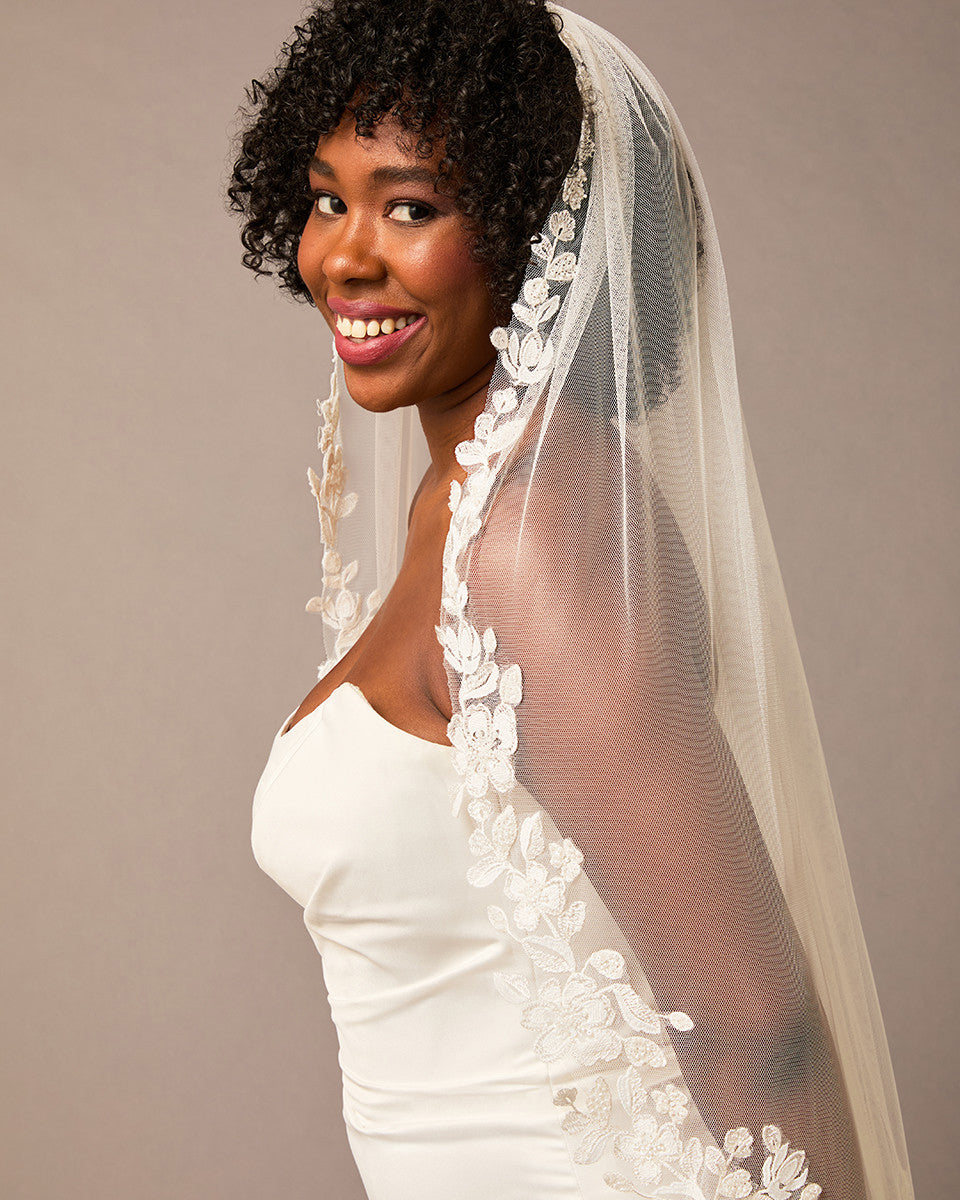 Ivory Luxe Tulle Lace Trim Royal Cathedral Bridal Veil Woman wearing a  wedding dress with a floral veil against a plain background