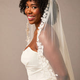 Ivory Luxe Tulle Lace Trim Royal Cathedral Bridal Veil Woman wearing a  wedding dress with a floral veil against a plain background