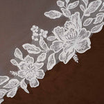 Cathedral Mantilla Wedding Veil Adorned with Lace Cassandra Lynne -floral lace trim with embroidered roses and leaves laid diagonally across a dark brown textured fabric background.