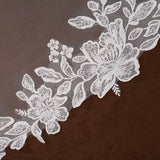Cathedral Mantilla Wedding Veil Adorned with Lace Cassandra Lynne -floral lace trim with embroidered roses and leaves laid diagonally across a dark brown textured fabric background.