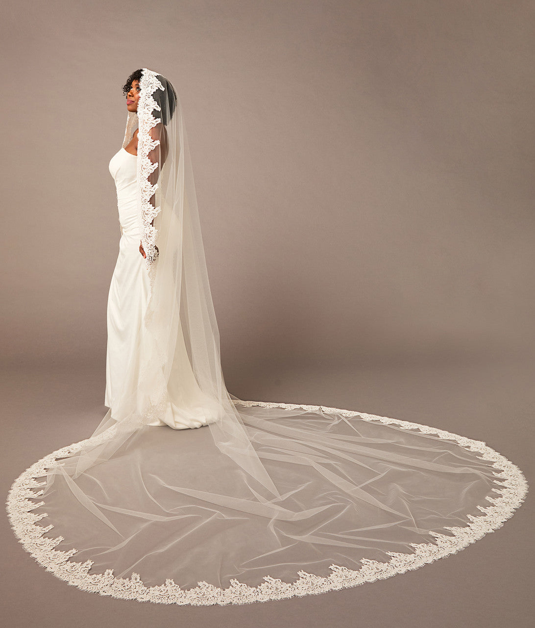 Bride wearing a long, elegant white wedding veil against a brown background Royal Cathedral Mantilla Veil with Wide Chantilly Lace