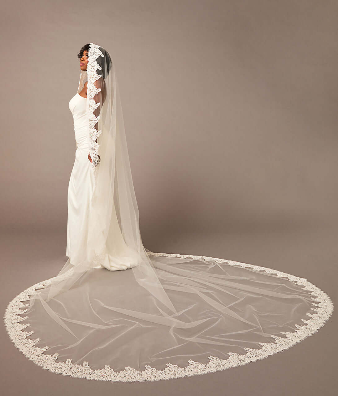 Bride wearing a long, elegant white wedding veil against a brown background Royal Cathedral Mantilla Veil with Wide Chantilly Lace