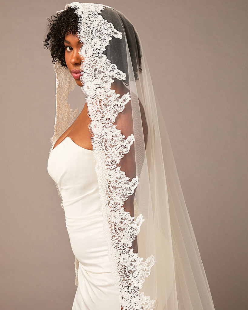 Woman wearing a white wedding dress with a lace veil against a plain Royal Cathedral Mantilla Veil with Wide Chantilly Lace background