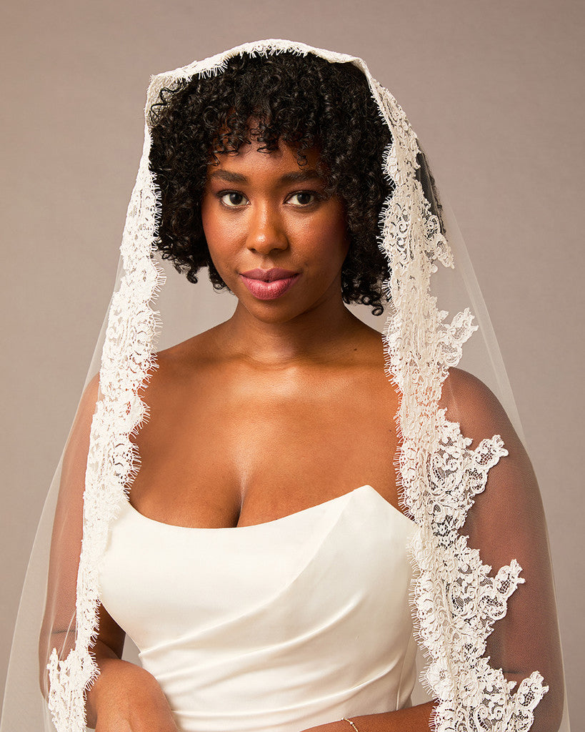 Woman wearing a white wedding dress with a lace veil against a neutral background Royal Cathedral Mantilla Veil with Wide Chantilly Lace