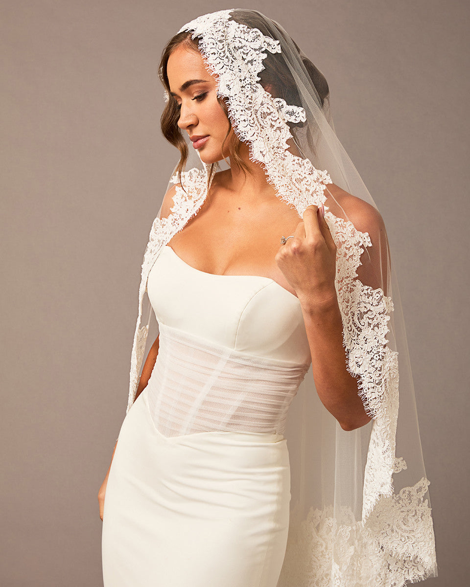 Woman wearing a white wedding dress with a lace veil against a neutral background Fingertip Mantilla Veil with Wide Chantilly Lace