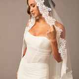 Woman wearing a white wedding dress with a lace veil against a neutral background Fingertip Mantilla Veil with Wide Chantilly Lace