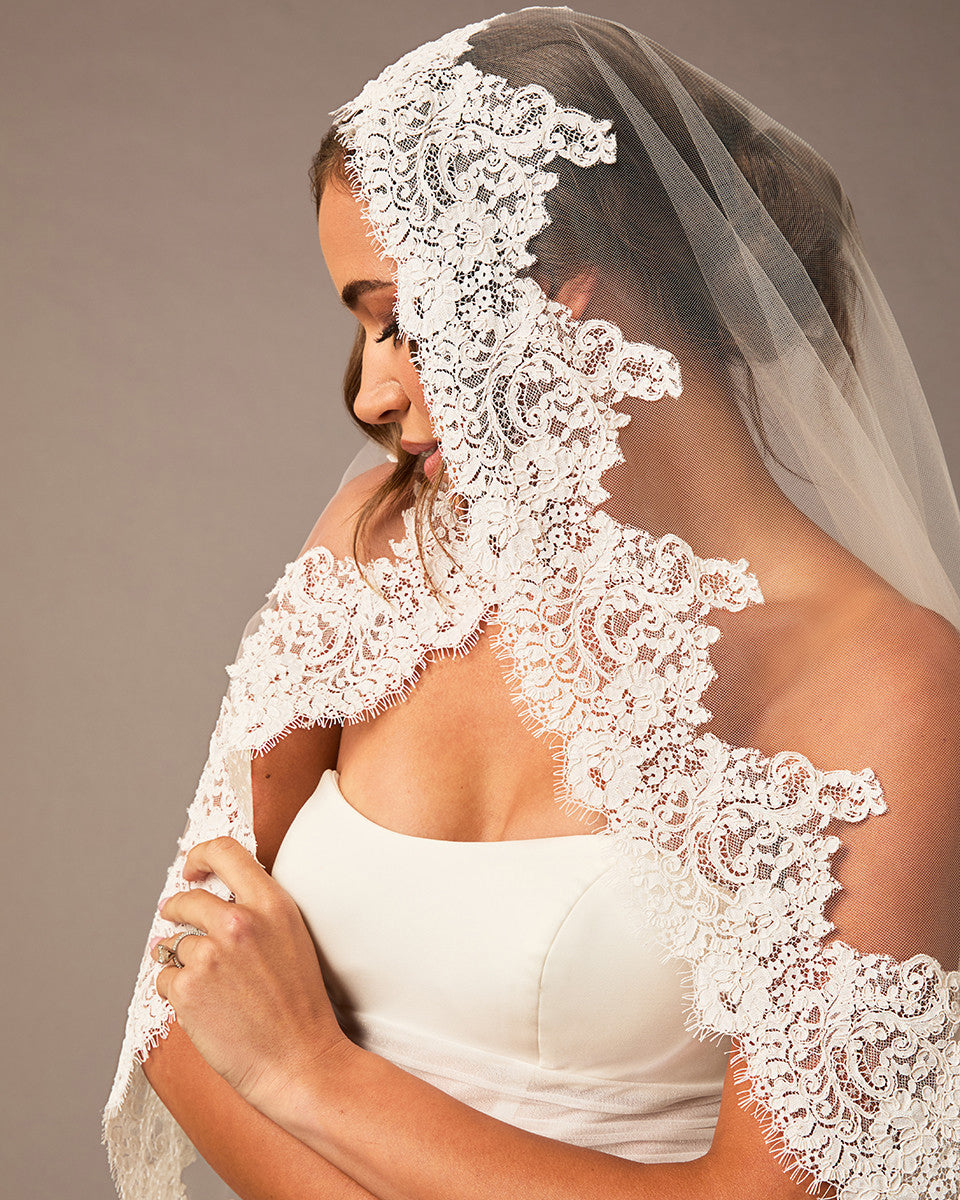 Bride wearing a lace veil against a neutral background Fingertip Mantilla Veil with Wide Chantilly Lace