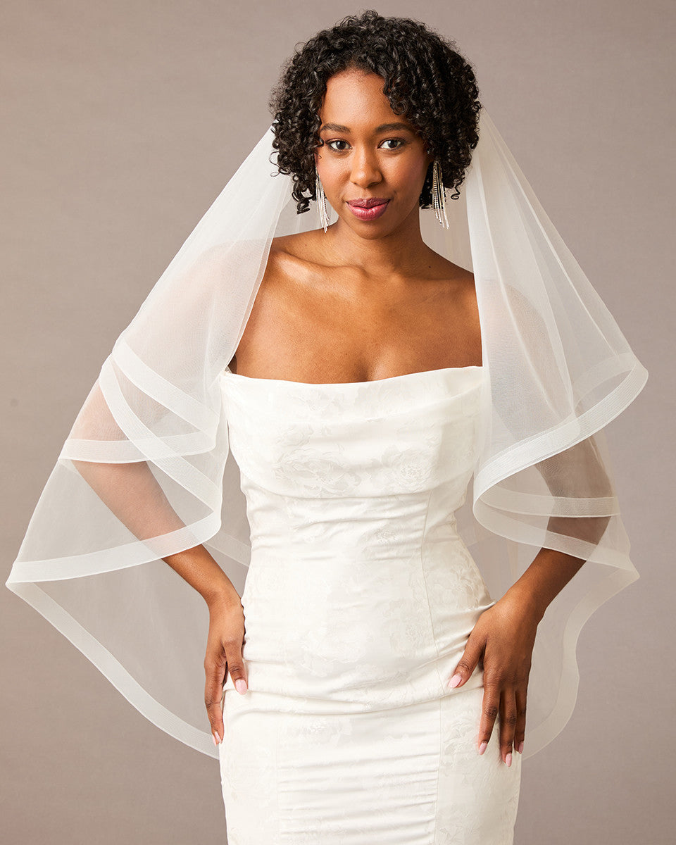 Fingertip Horsehair Trim Two Layer Wedding Veil Woman wearing a wedding dress with a sheer white veil against a neutral background
