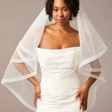 Fingertip Horsehair Trim Two Layer Wedding Veil Woman wearing a wedding dress with a sheer white veil against a neutral background