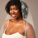 Royal Mantilla Veil with Pearl Clusters and Scatter Woman wearing a  wedding dress and veil with floral details against a neutral background