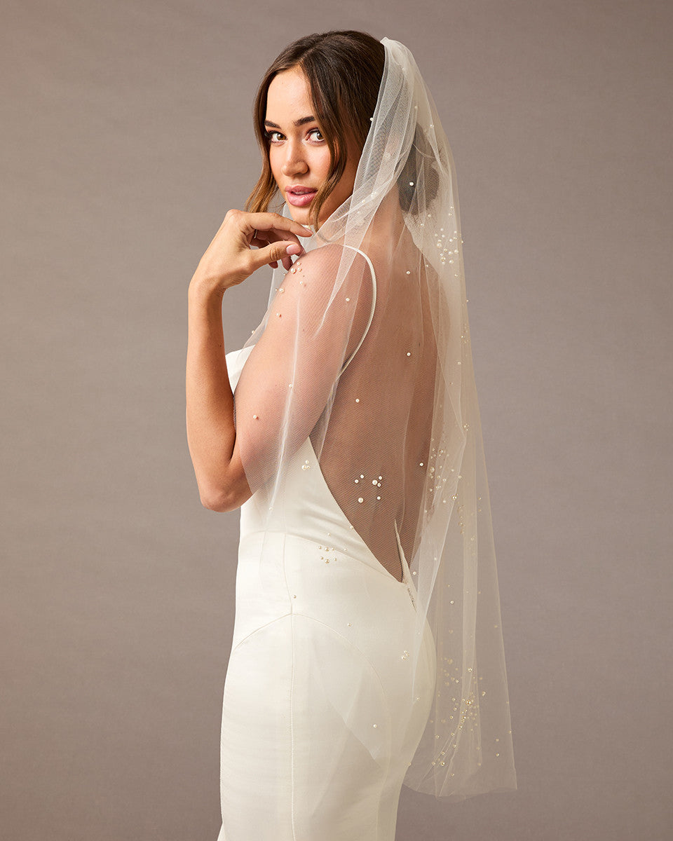 Fingertip Veil with Scattered Dense Pearl Clusters Woman wearing a wedding dress with a sheer veil against a plain background