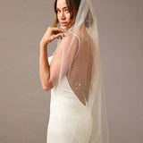Fingertip Veil with Scattered Dense Pearl Clusters Woman wearing a wedding dress with a sheer veil against a plain background