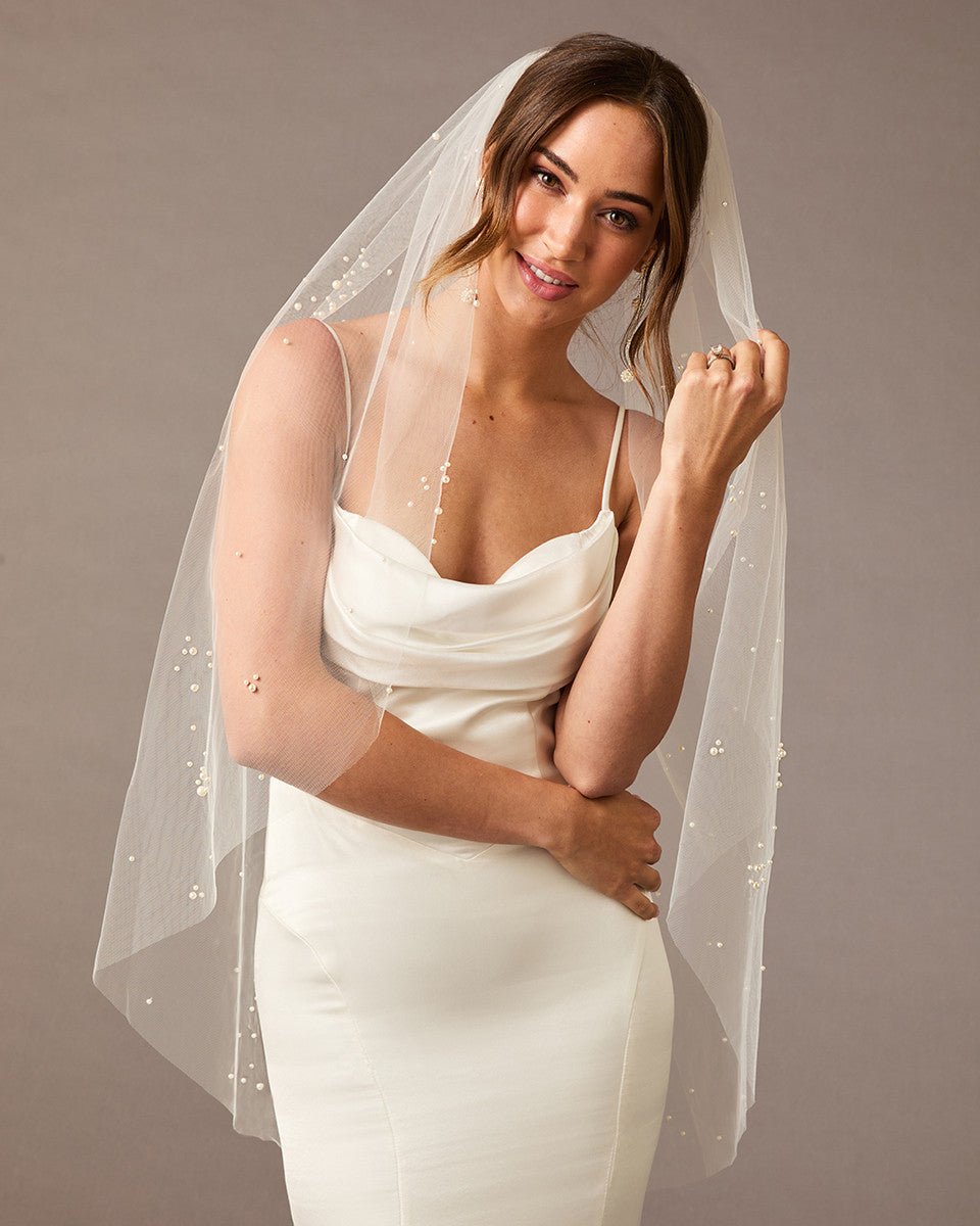 Fingertip Veil with Scattered Dense Pearl Clusters Woman wearing a wedding dress with a veil against a plain background