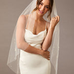 Fingertip Veil with Scattered Dense Pearl Clusters Woman wearing a wedding dress with a veil against a plain background