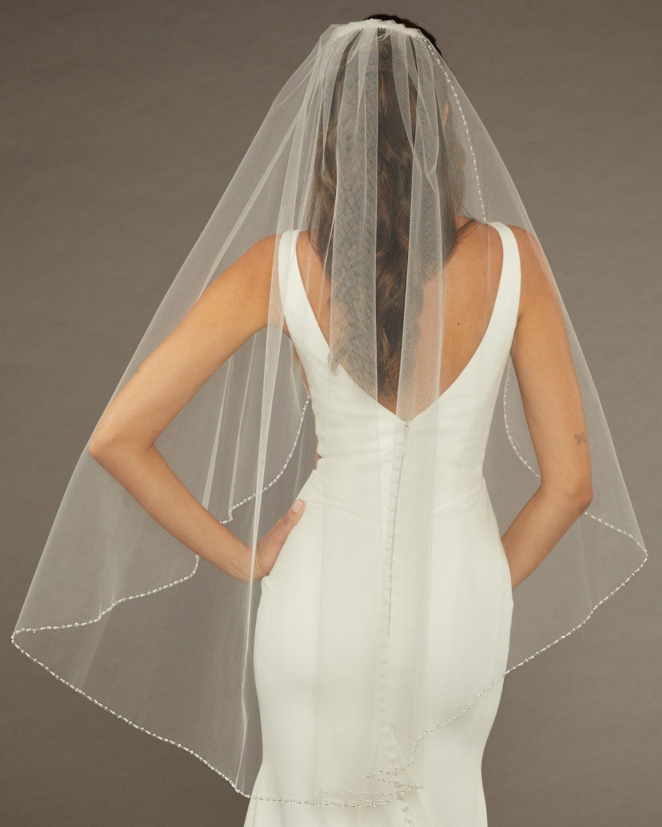 Fingertip Veil with Pearls and Sequins Bride wearing a  wedding dress with a sheer veil against a brown background