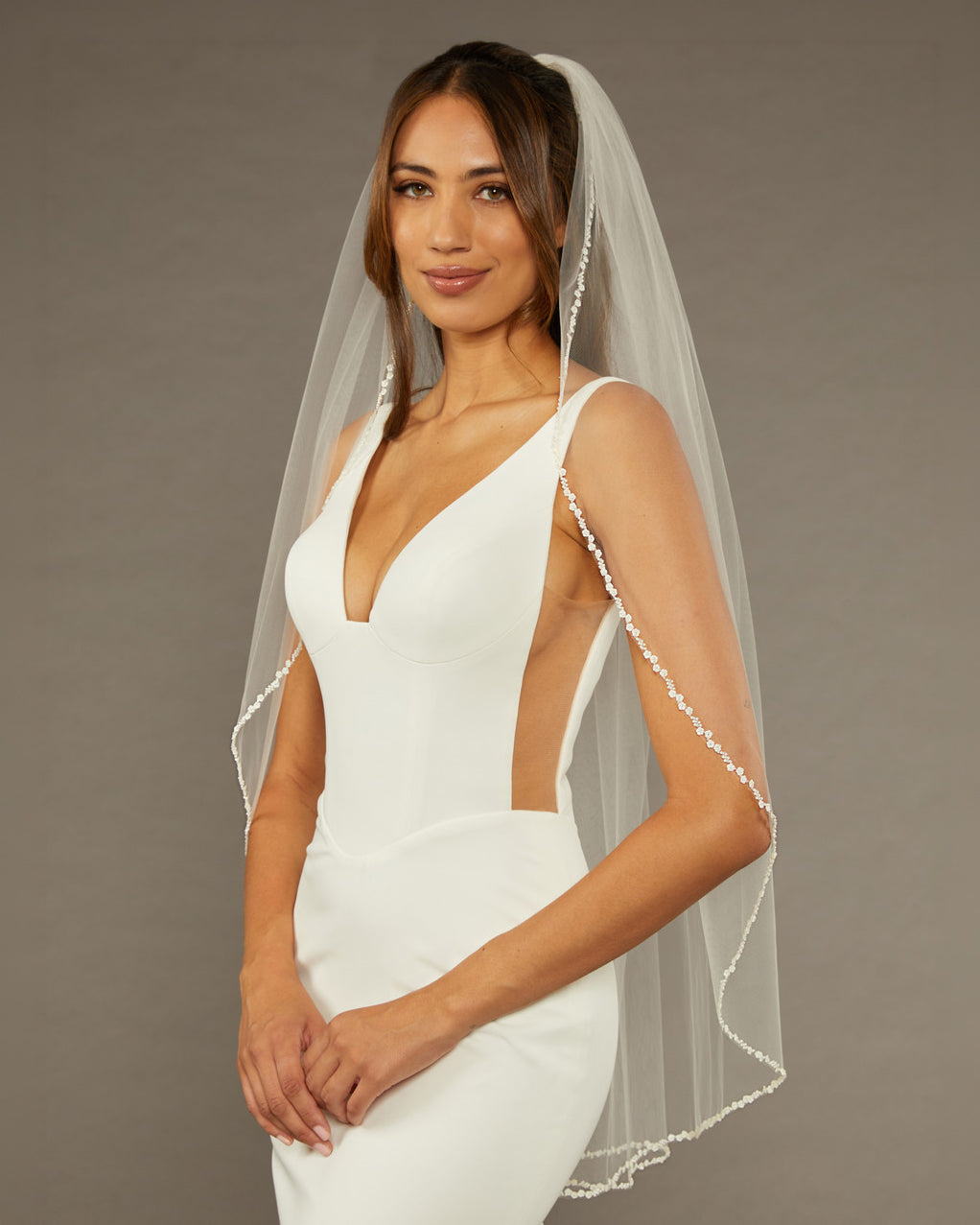 Metal Flower and Beads Fingertip Bridal Veil Woman wearing a  wedding dress with a sheer veil against a brown background