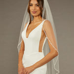 Metal Flower and Beads Fingertip Bridal Veil Woman wearing a  wedding dress with a sheer veil against a brown background