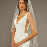 Metal Flower and Beads Fingertip Bridal Veil Woman wearing a  wedding dress with a sheer veil against a brown background