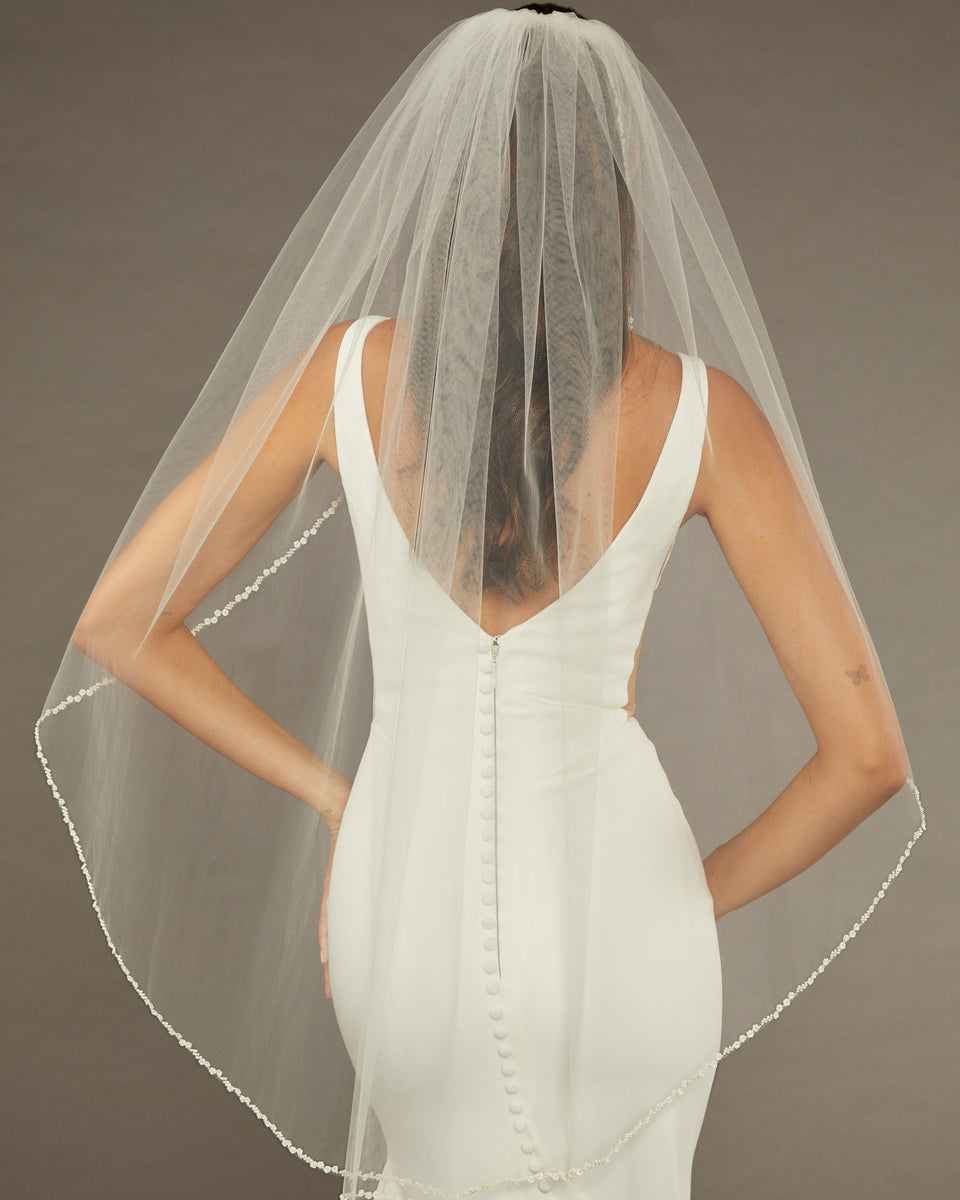 Metal Flower and Beads Fingertip Bridal Veil Bride wearing a  wedding dress with a sheer veil against a neutral background